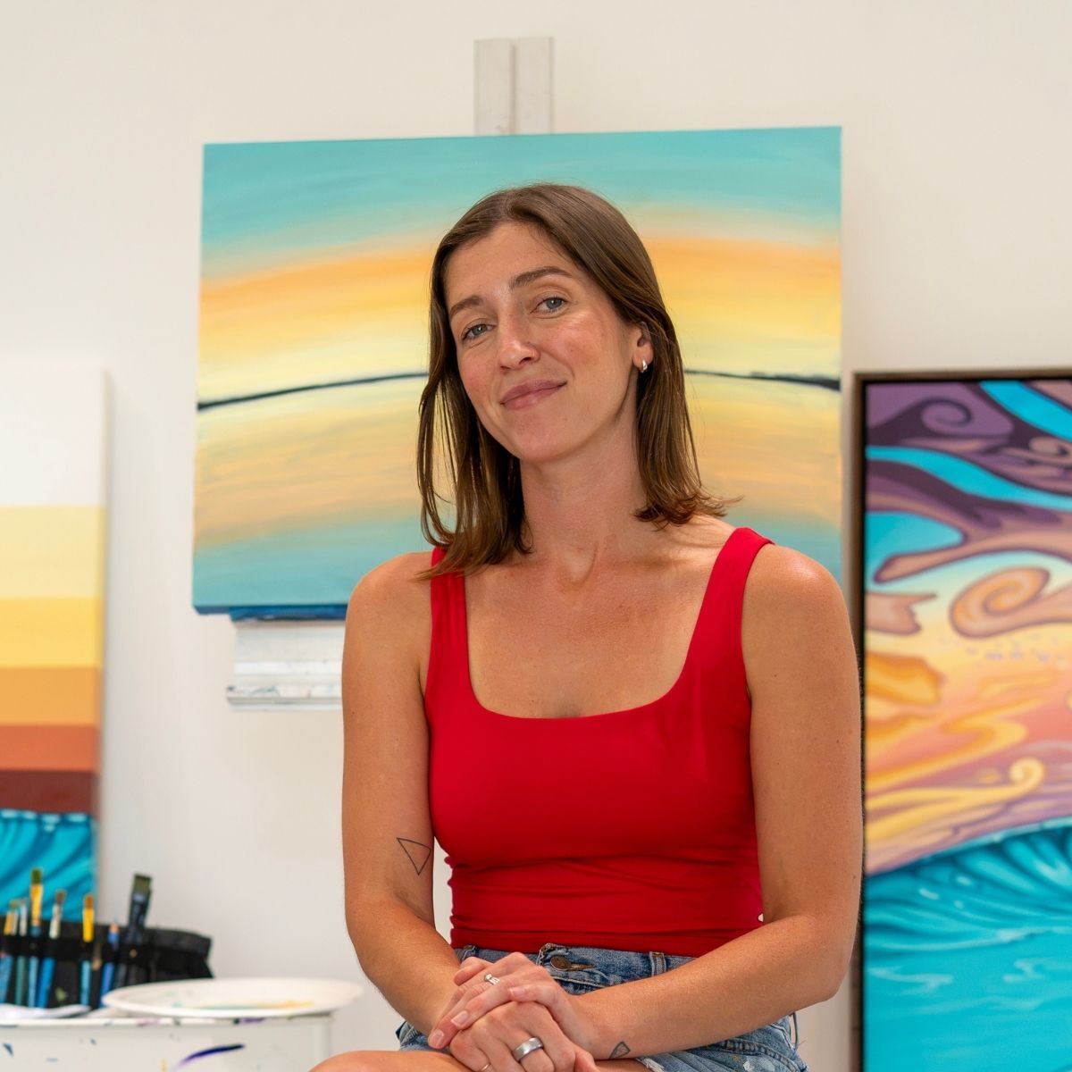 A photo of artist Gianna Andrews in here studio among her paintings.