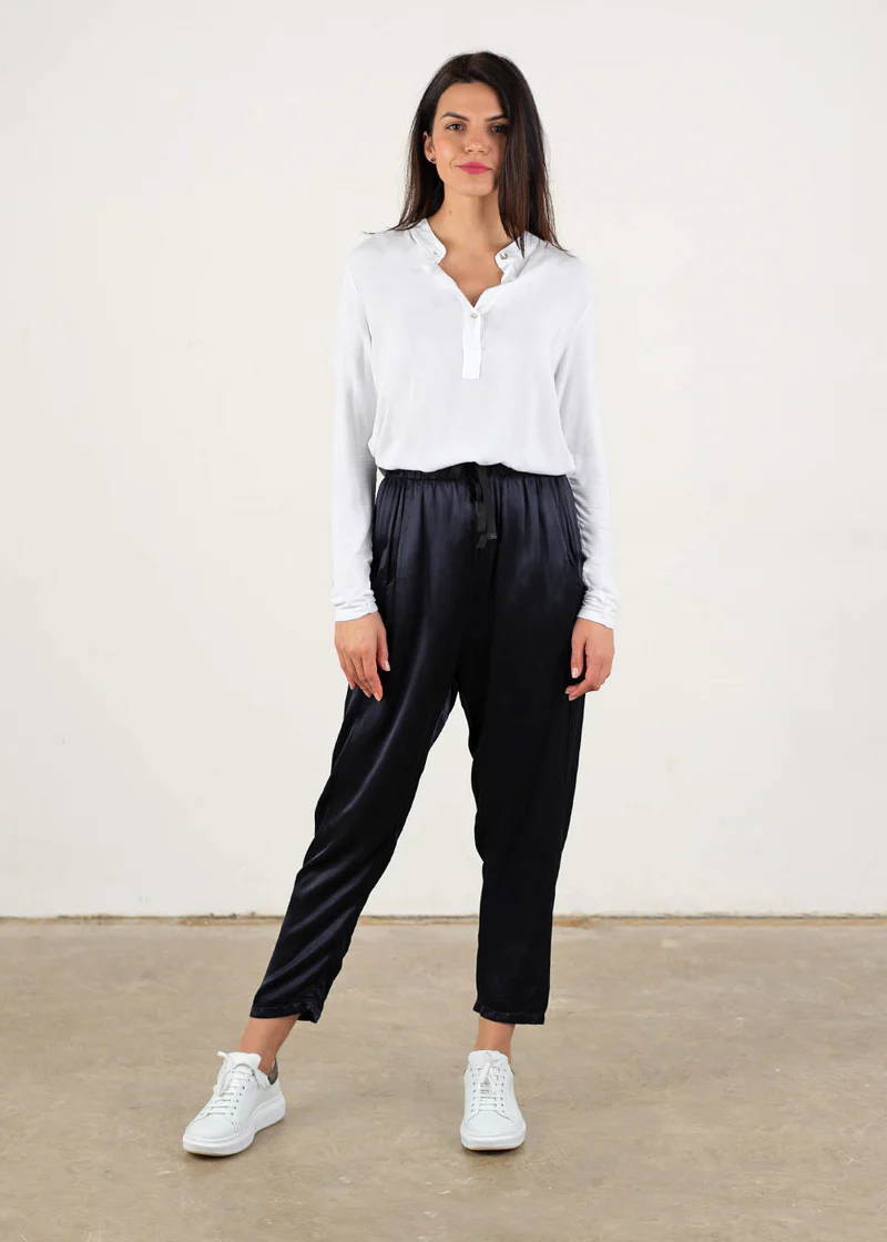 A model wearing a white long sleeve blouse with blue black satin trousers and white trainers