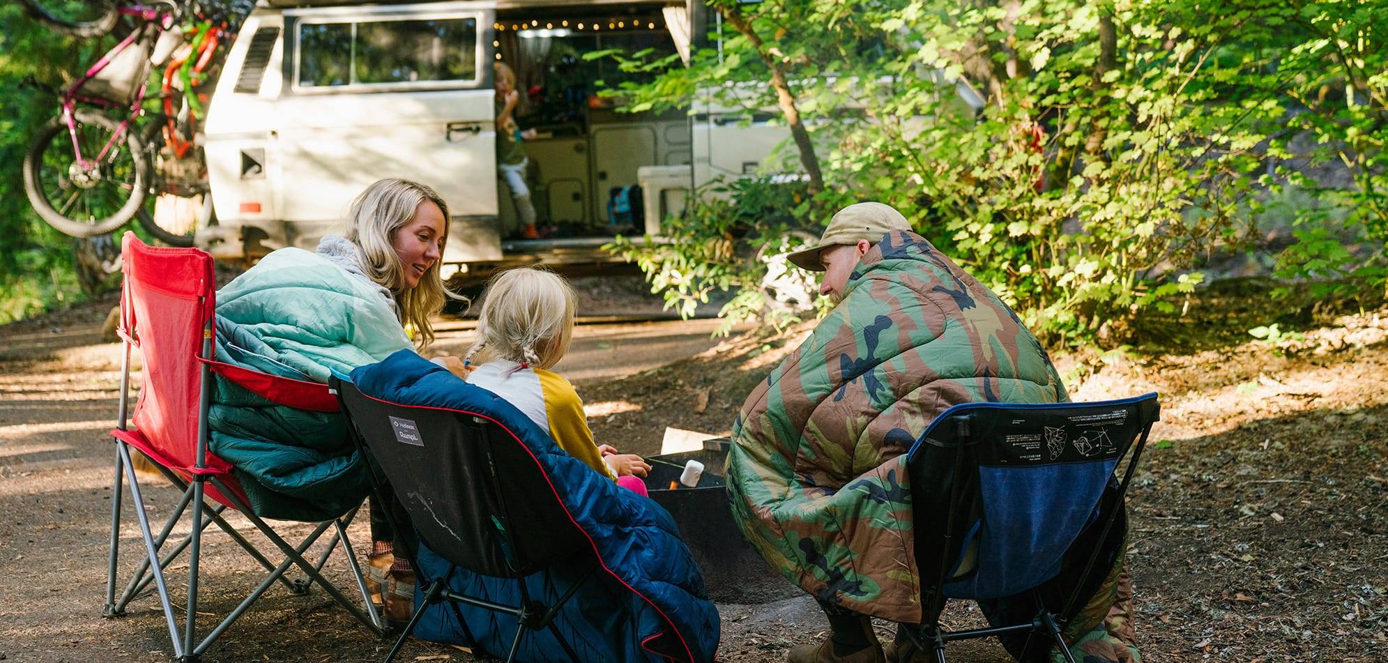 Family sitting around a campfire with camping blankets