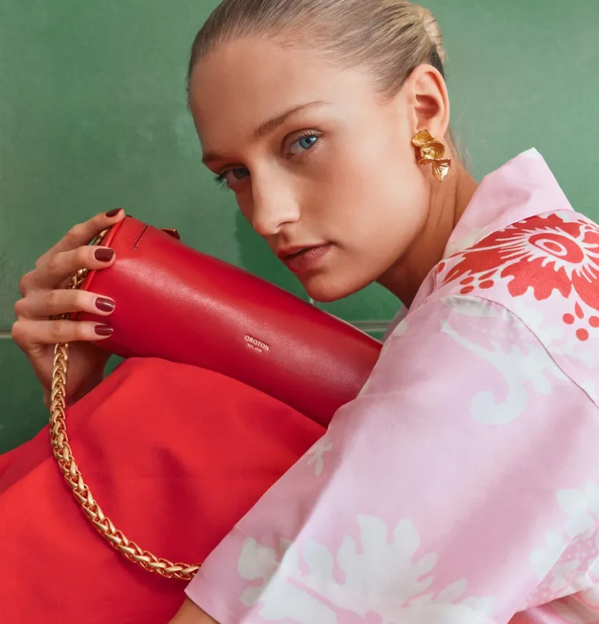 Woman in a floral shirt holding a red handbag against a green background.