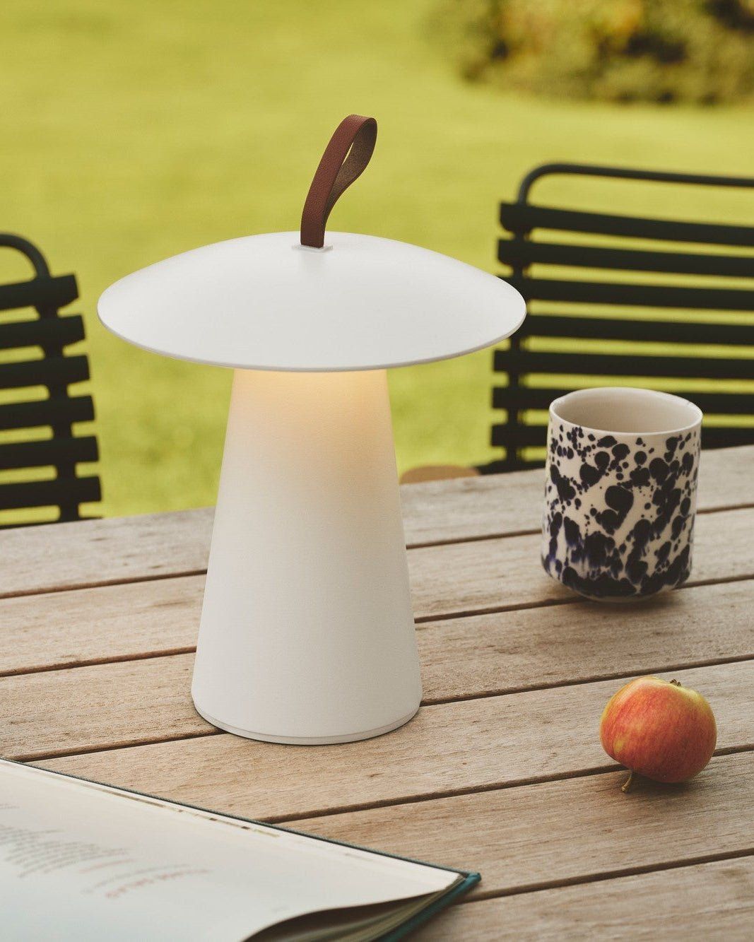 White outdoor lamp on a wooden table with apples and a cup in a garden setting - Lighting Collective 