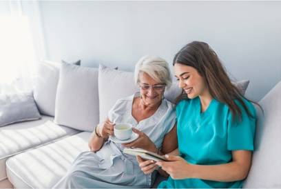 Nurse with older patient on a couch reading a book or journal. 