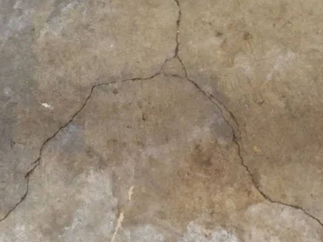 Using a grinder and diamond blade to widen cracks in the floor, preparing it for material filling.