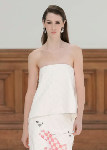Model wearing a strapless white top and floral skirt on the runway.