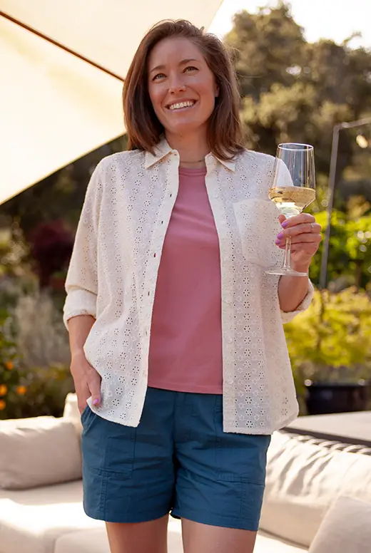 Smiling woman holding a glass of wine outdoors, wearing casual summer clothing.