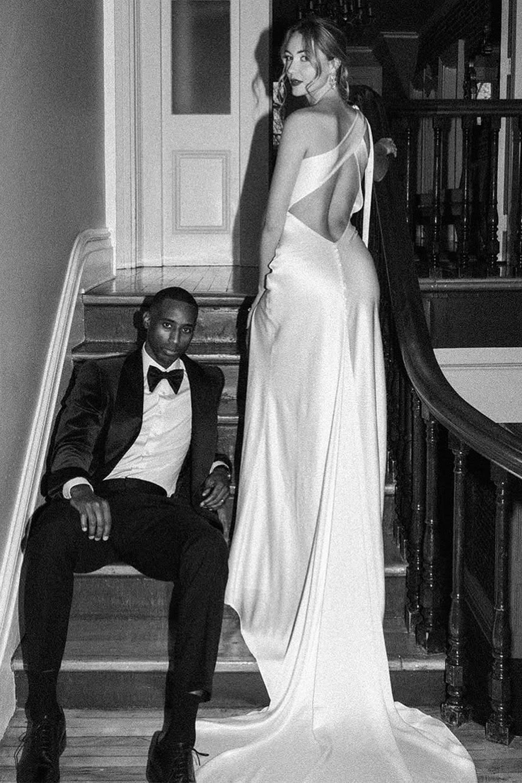 A man in a tuxedo sits on stairs beside a woman in a white dress.