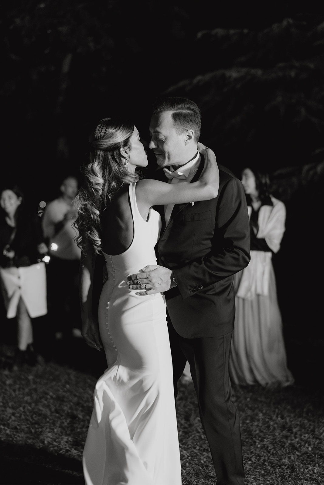 A couple dances romantically at a wedding reception under dim lighting.