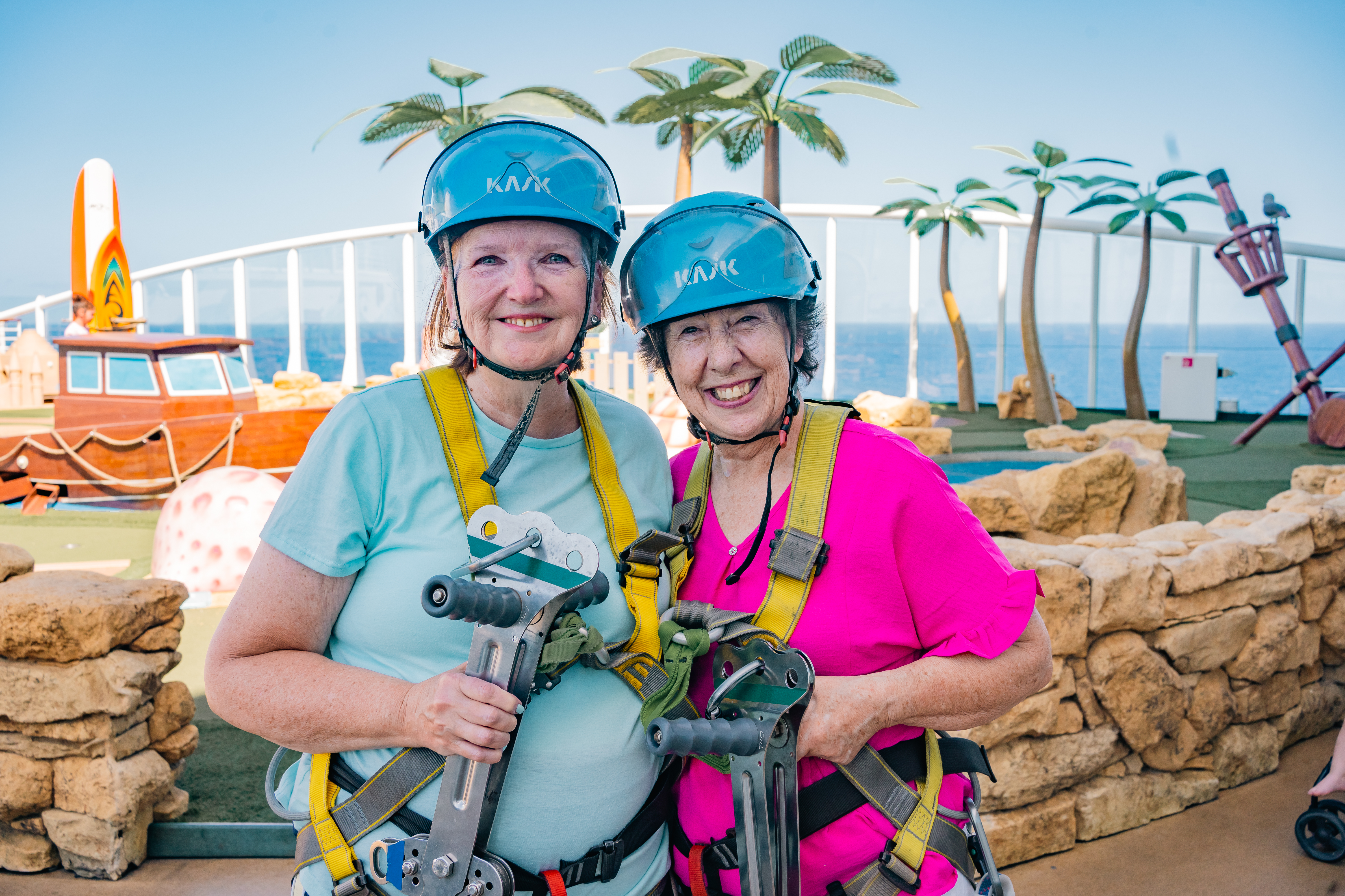 Two women in helmets smiling, posing in a recreational outdoor setting.