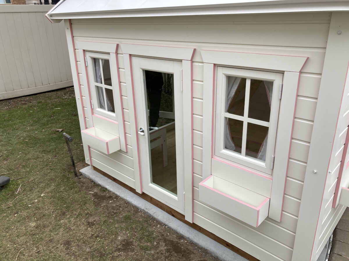 Custom playhouse white front with glass door and windows on grass by WholeWoodPlayhouses