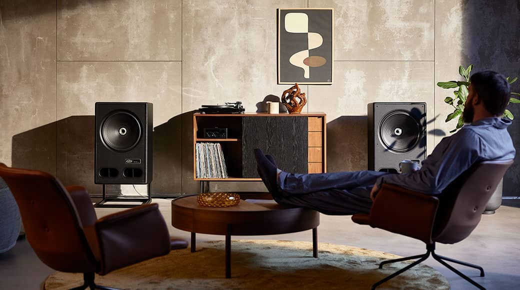 Person relaxing in a stylish room with speakers and furniture.