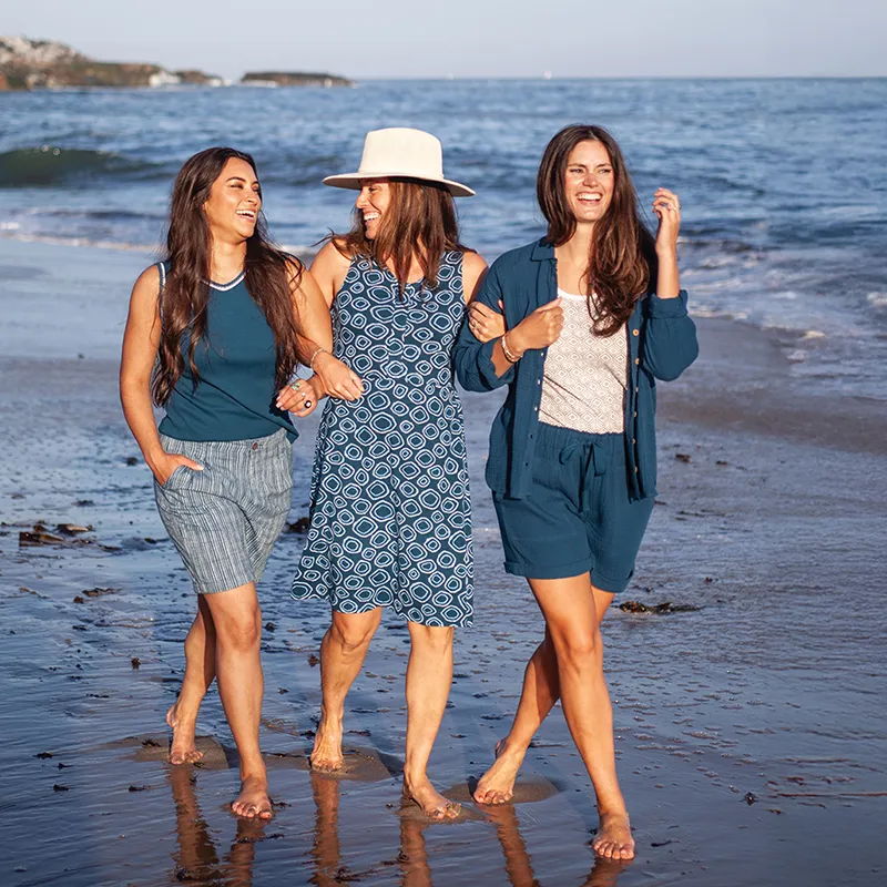 Three women walking on the beach in casual summer outfits.