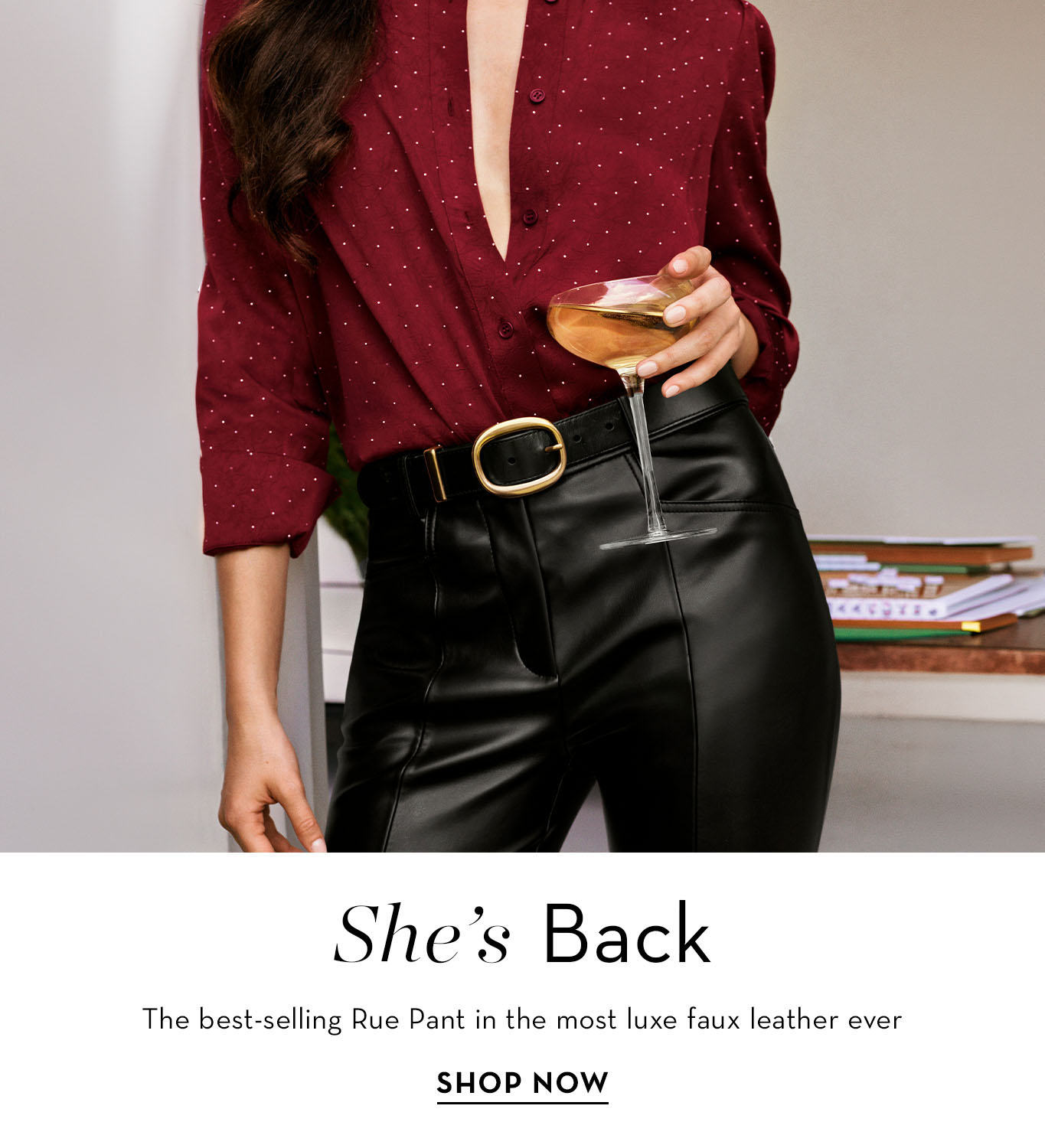 Woman in a burgundy shirt and black faux leather pants holding a drink.