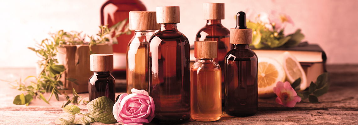 Glass bottles of essential oils and herbs on a wooden surface.