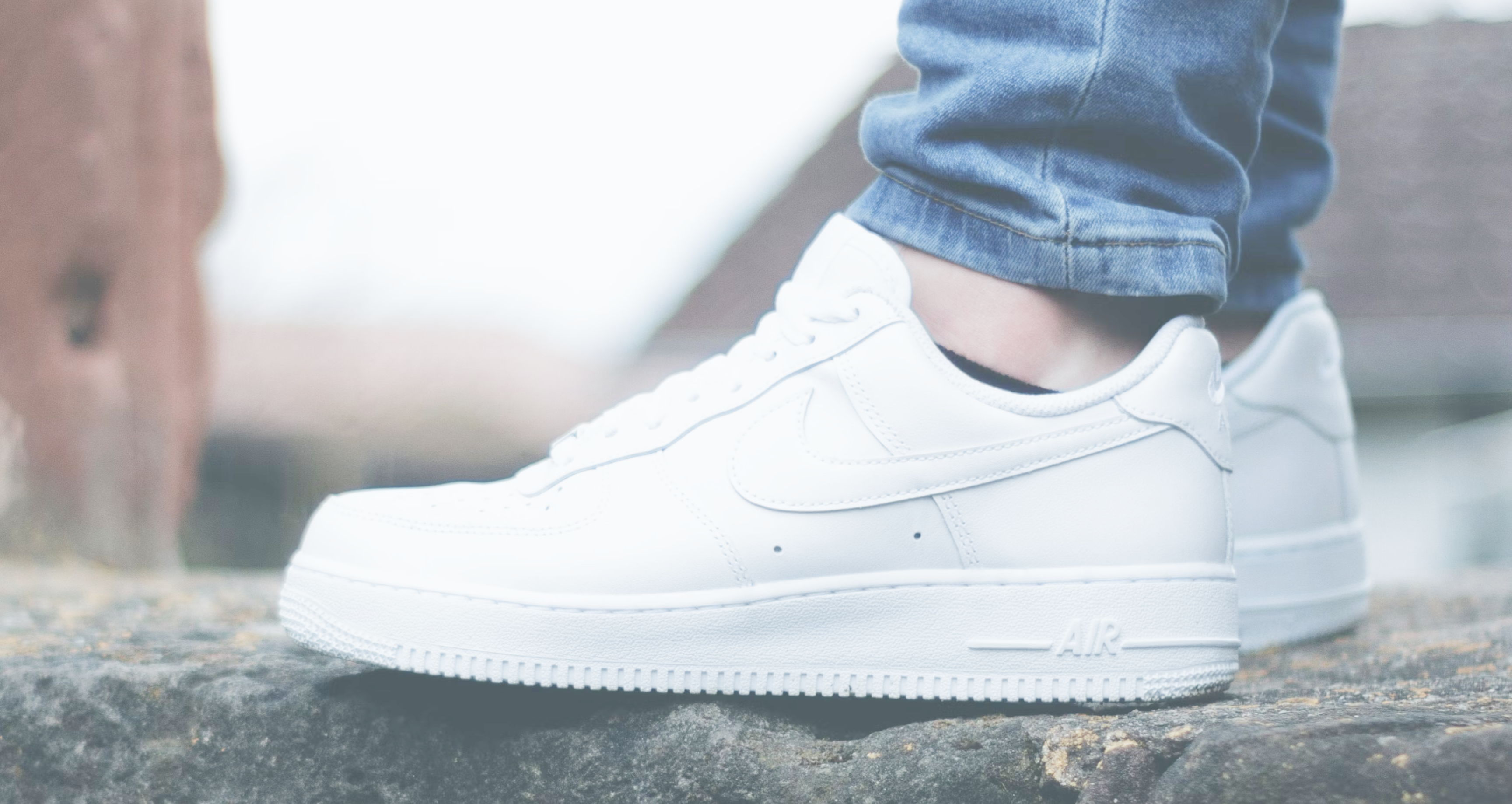 A person wearing white sneakers and blue jeans while standing on a stone step