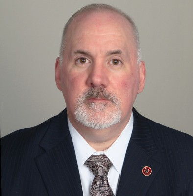 Professional man in a suit with a serious expression against a neutral background.