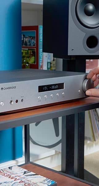 A person adjusting a silver audio receiver on a wooden shelf.
