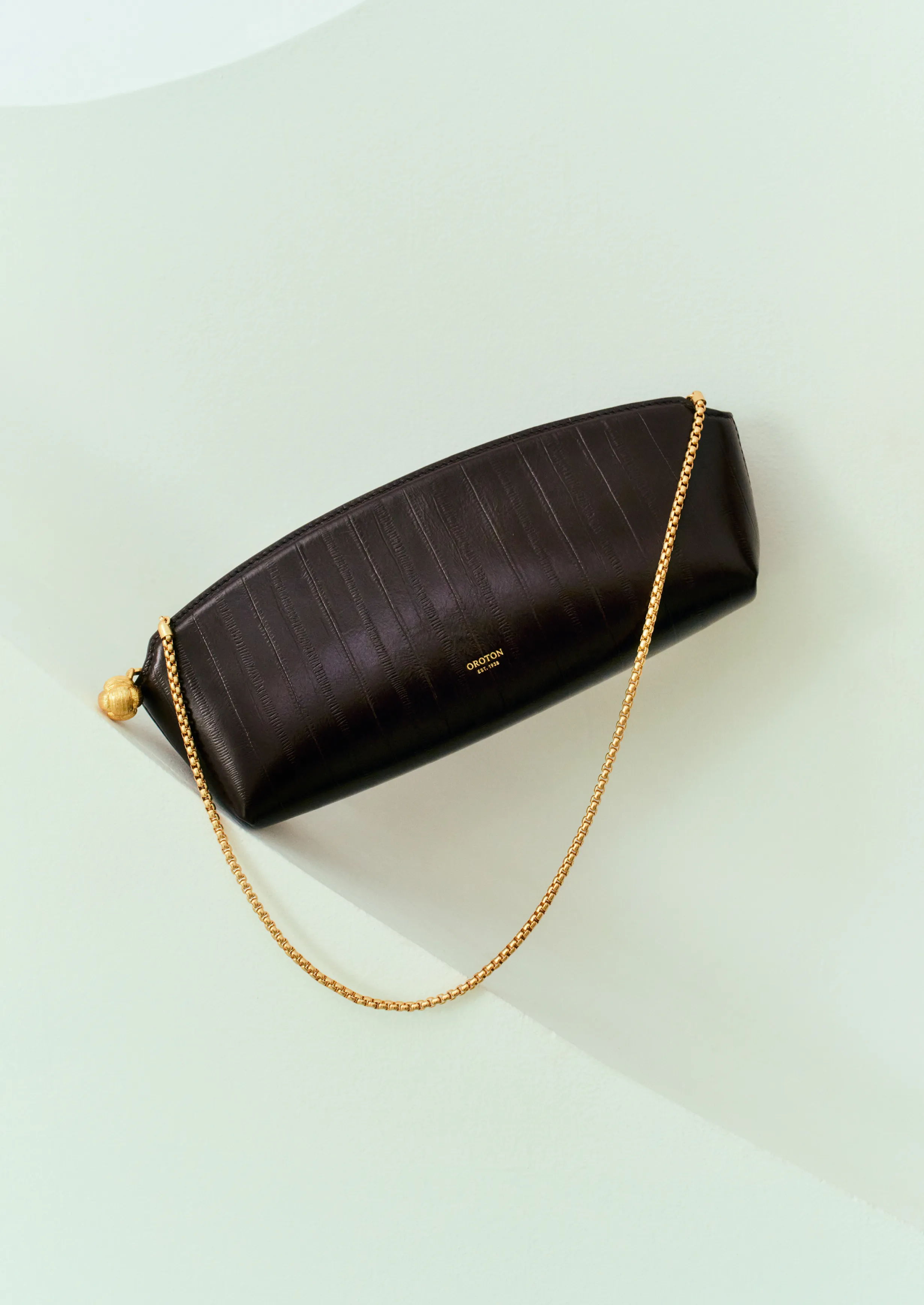 A dark brown handbag with a gold chain on a light background.