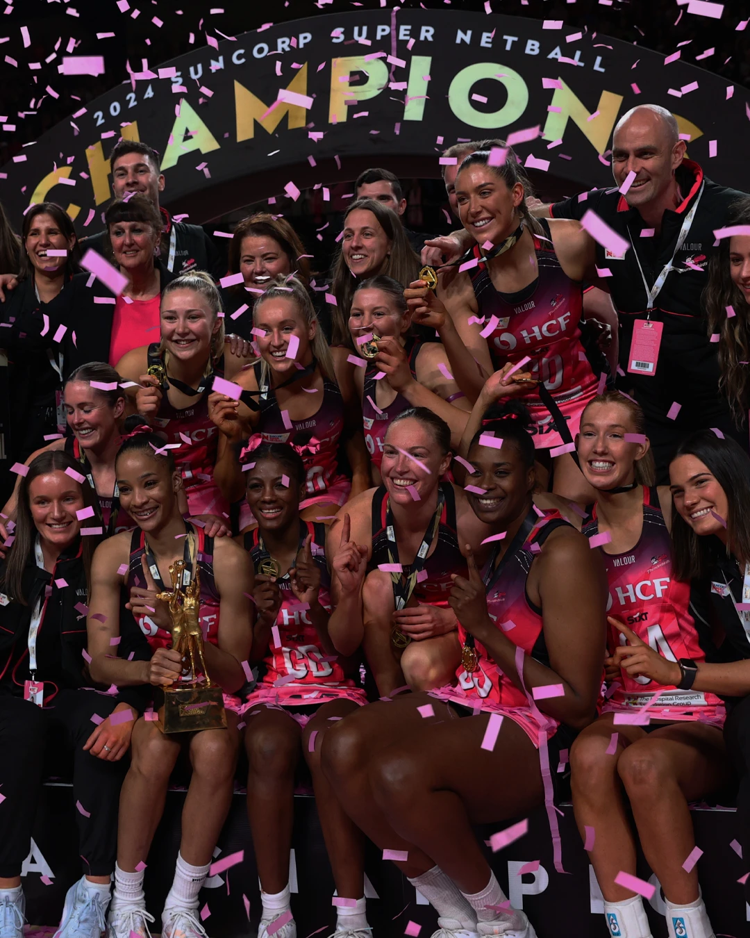 Netball team celebrating victory with trophies and confetti.