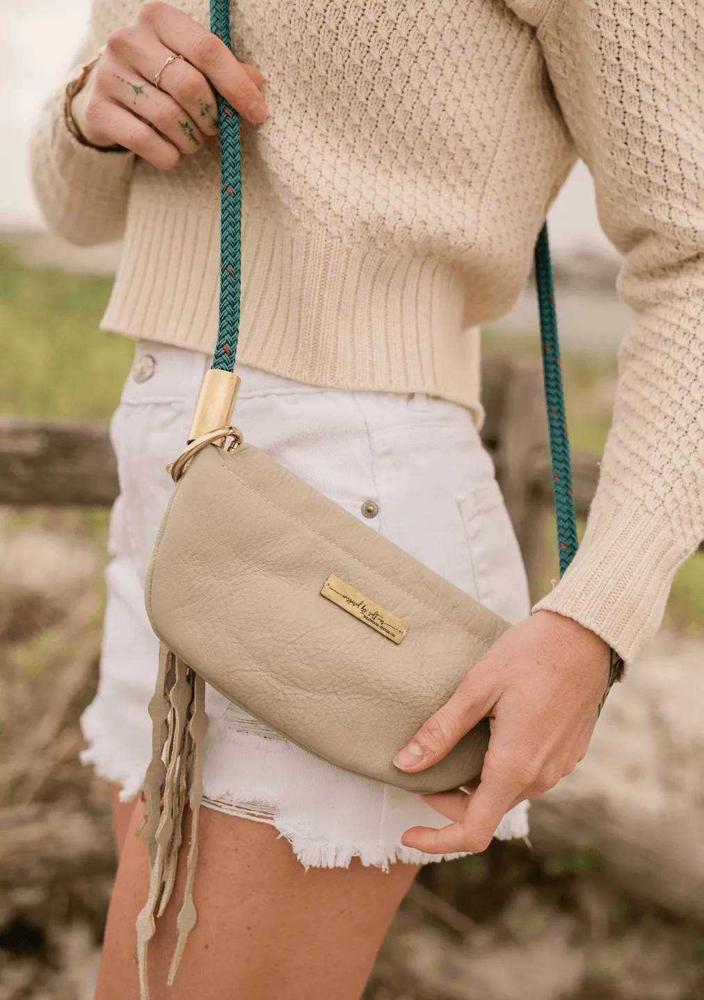 woman wearing a beige leather bag with a brass taglet