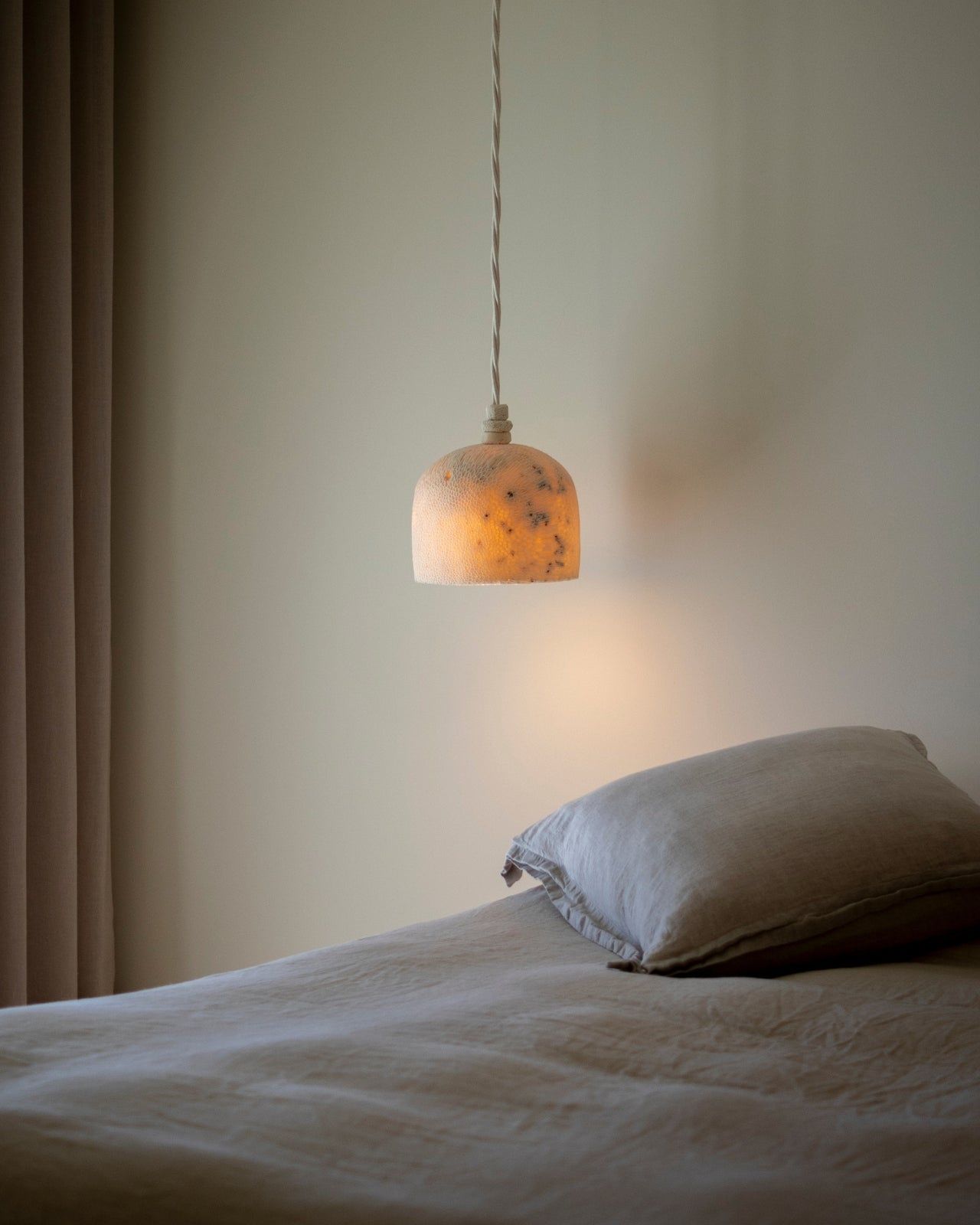 Bed with a pillow and a hanging lamp casting a warm glow in a bedroom setting.