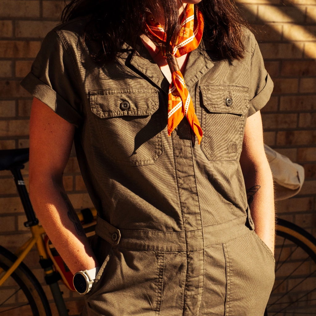 Person wearing a green jumpsuit and orange scarf, standing near a bicycle.