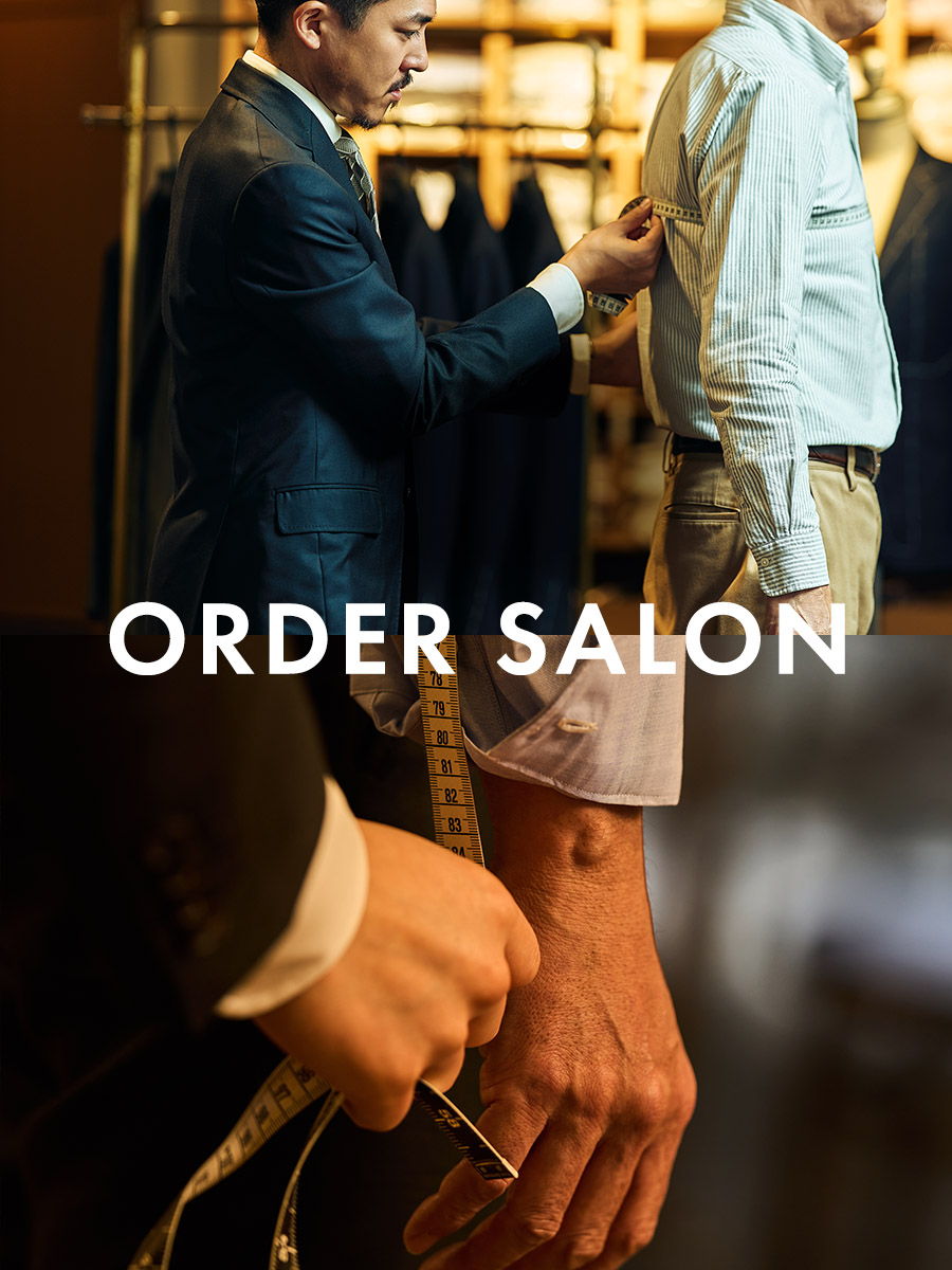 Tailor measuring a client for a custom suit in a stylish shop setting.