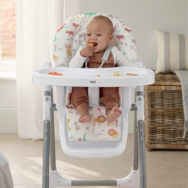 A happy baby sitting in a high chair, eating snacks.