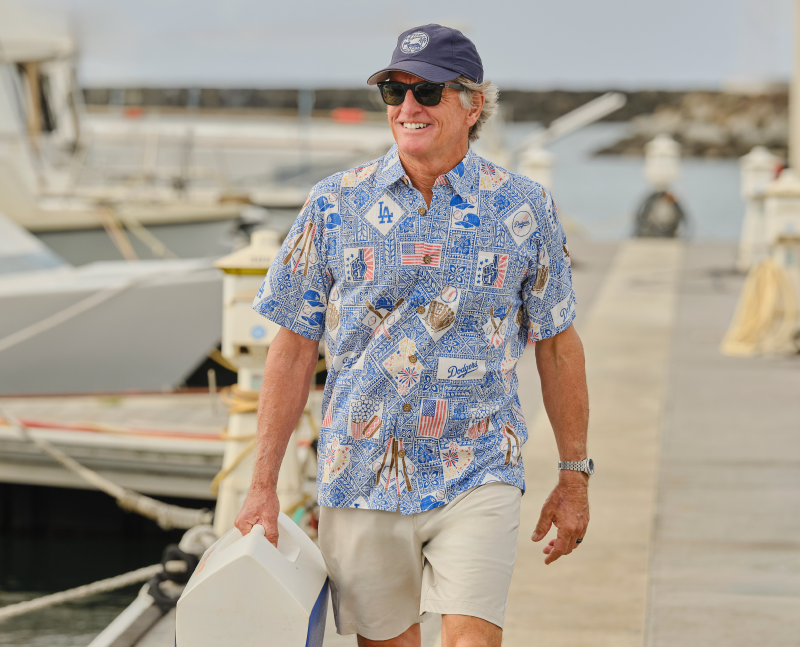 A man in a floral shirt walking by boats at a marina.