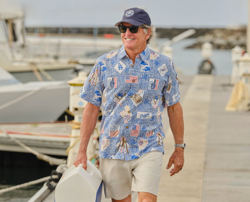 A man in a floral shirt walking by boats at a marina.