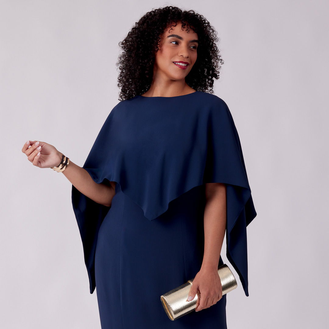 Woman in a navy dress holding a gold clutch, smiling confidently.