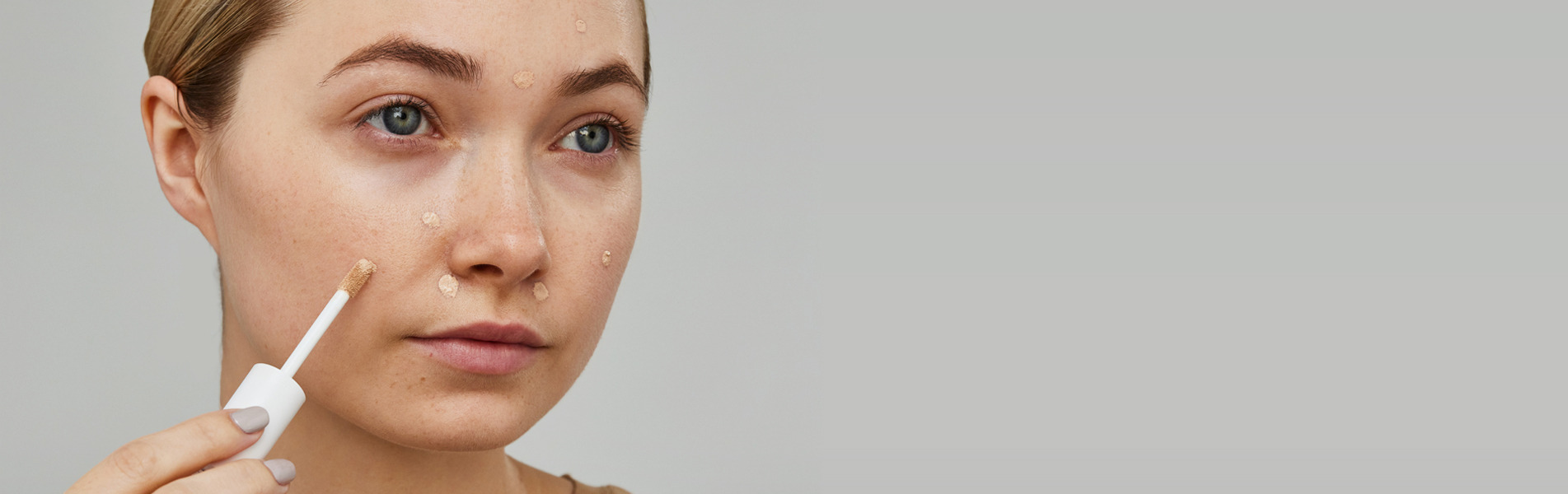 Woman applying serum to her face in a minimalistic setting.
