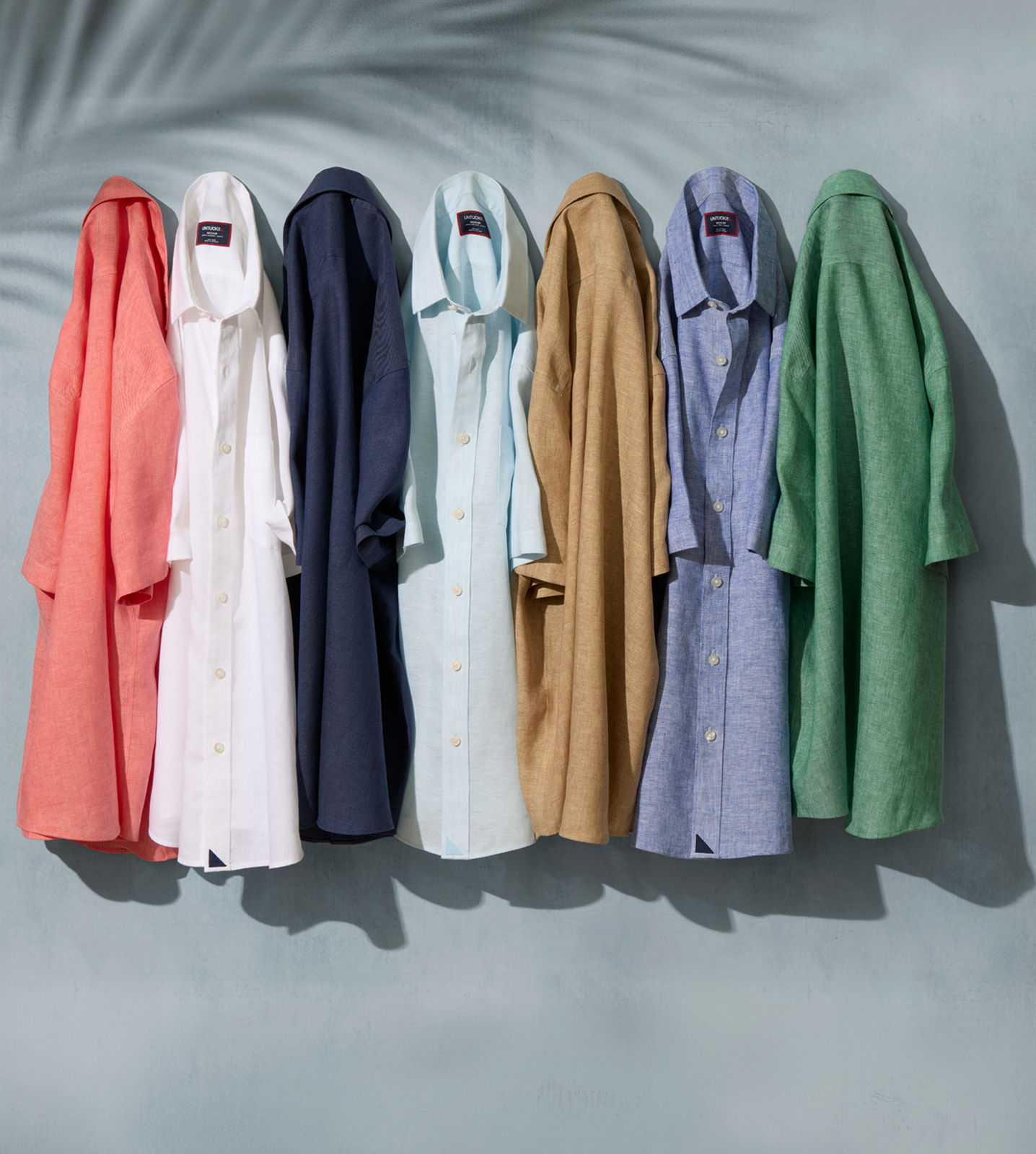 Seven shirts in various colors hanging against a textured background.