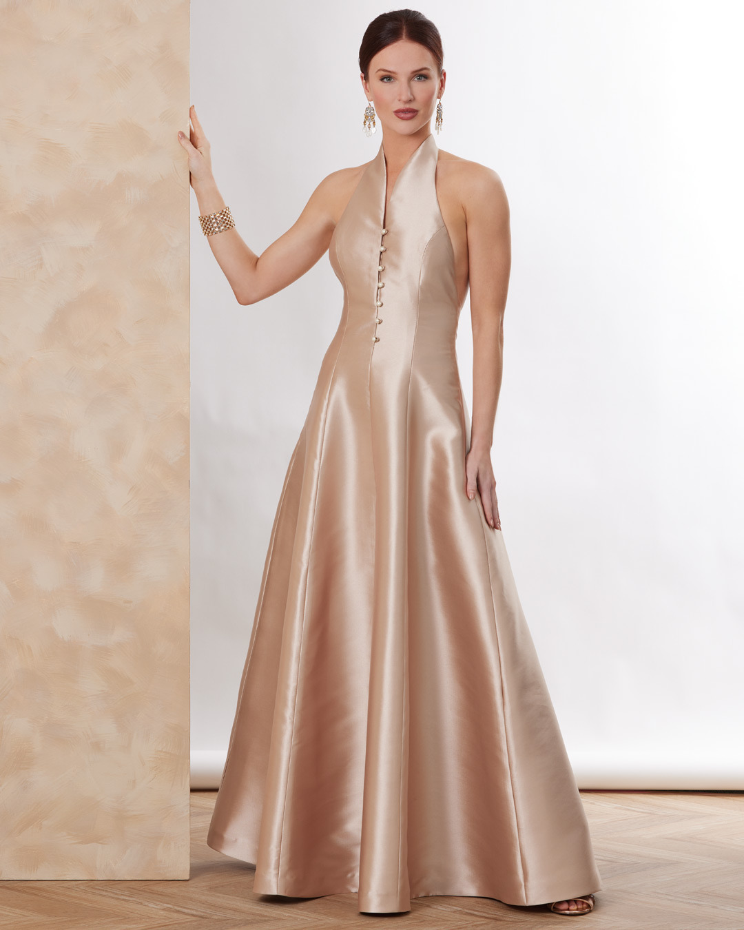 Woman in a halter neck satin gown standing elegantly against a neutral background.