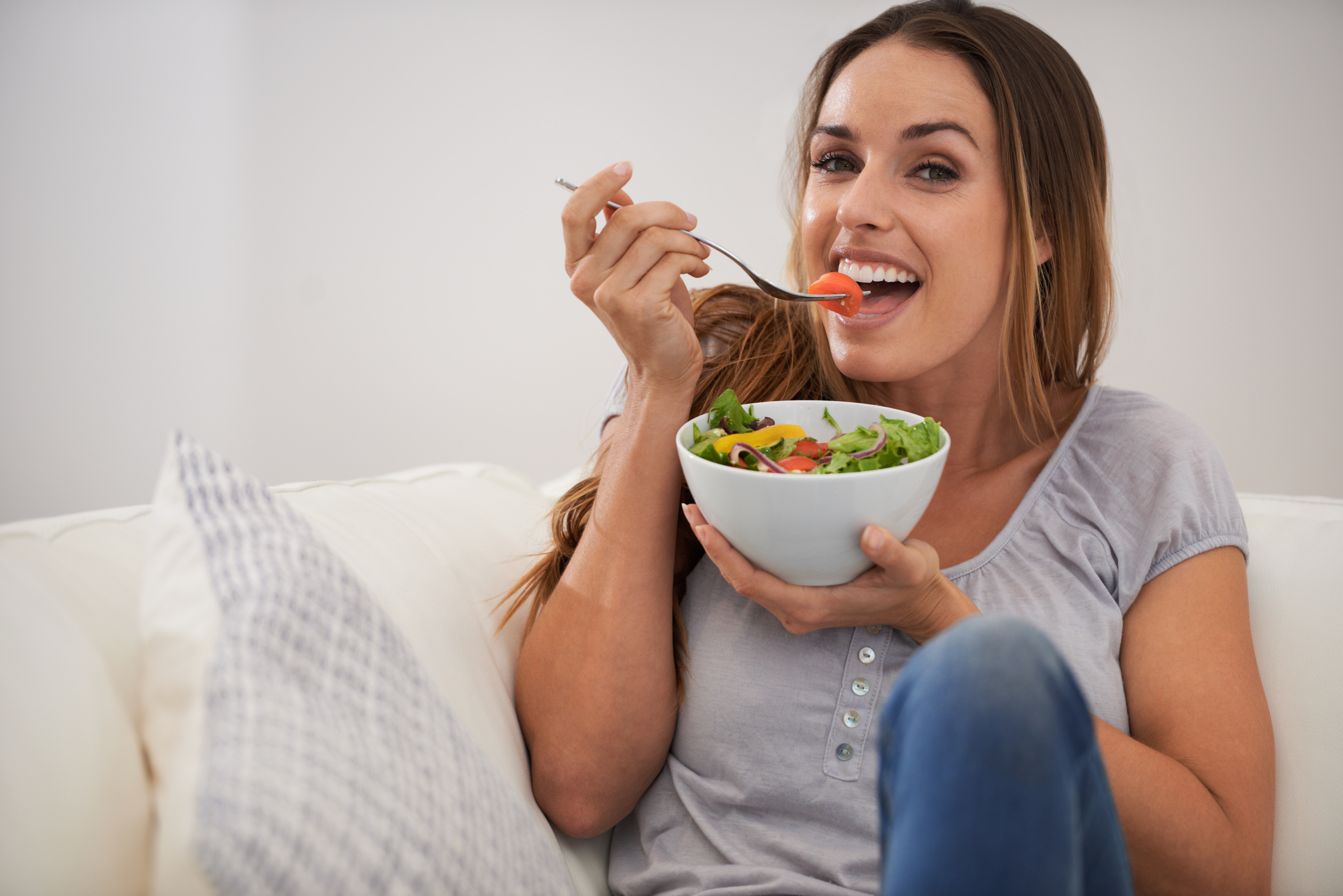 Woman enjoying a bowl of salad while sitting on a couch.