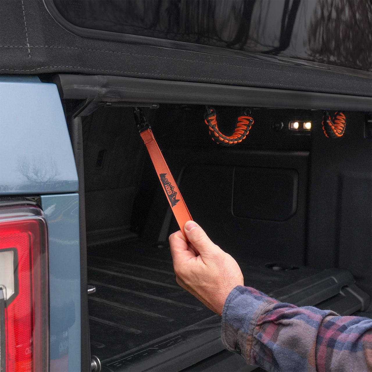 A hand holding an orange strap inside a truck bed.