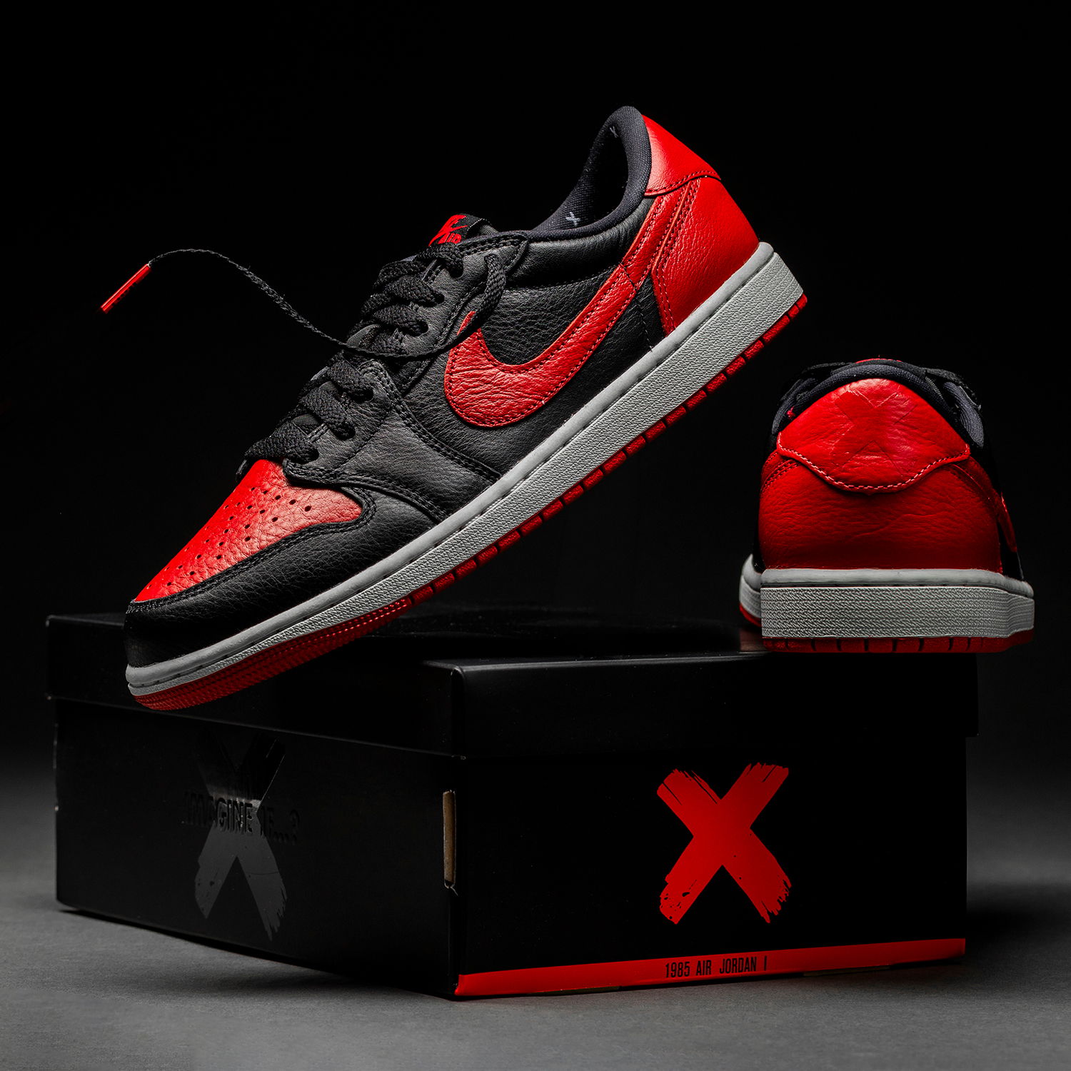 A stylish black and red sneaker on a box with a logo.