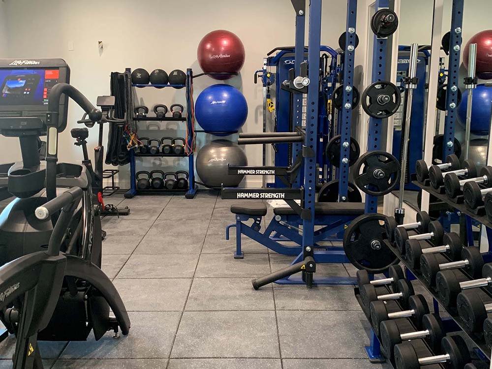 Home gym with blue Hammer Strength squat rack, Life Fitness Arc Trainer, dumbbells, and more fitness accessories