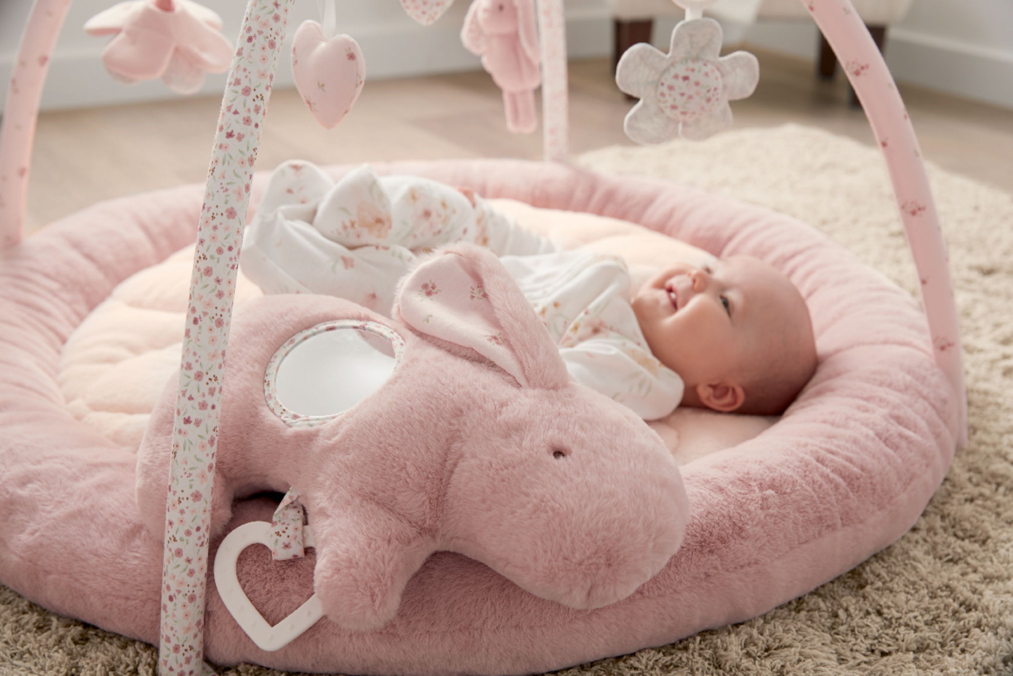 Baby lying on a pink play mat with hanging toys.