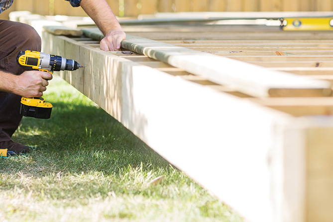 A person using a screwdriver in a garden to create a raised deck.
