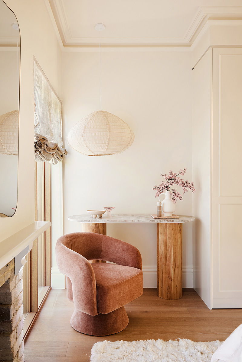A cozy interior with a pink chair, wooden table, and decorative lamp.