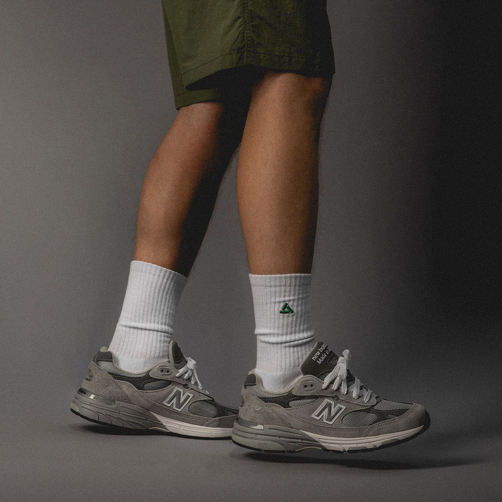 A person wearing gray New Balance sneakers and white socks with shorts.