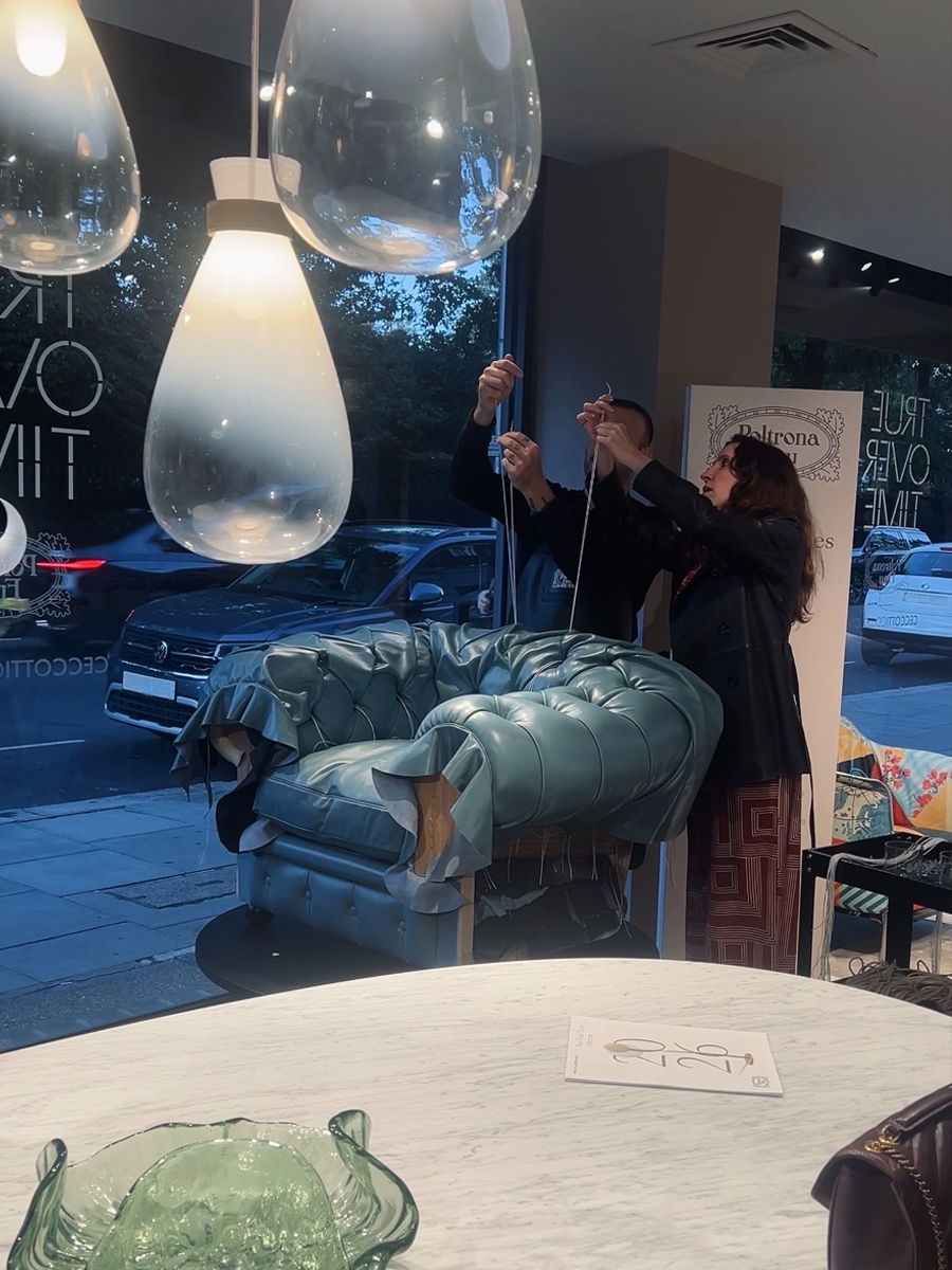 Two people making a Chester chair in the Poltrona Frau london showroom under hanging light fixtures.