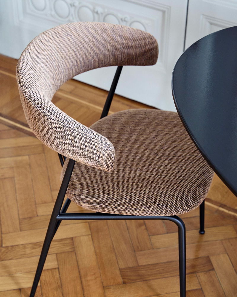 A modern Gubi chair with a curved backrest beside a round table.