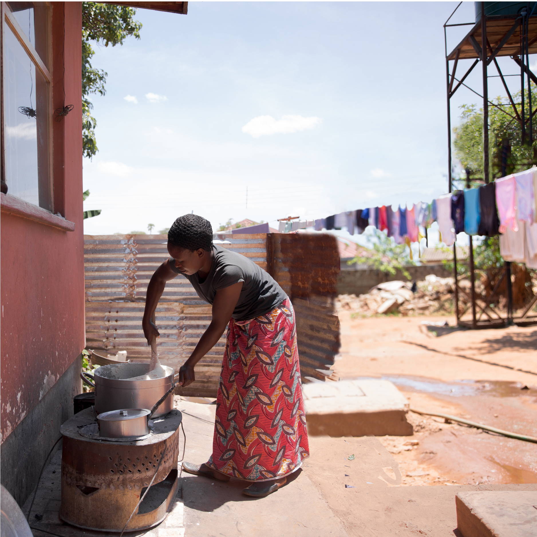 A Zambian woman stands outside cooking and stirring a large pot of nshima for small children.  
