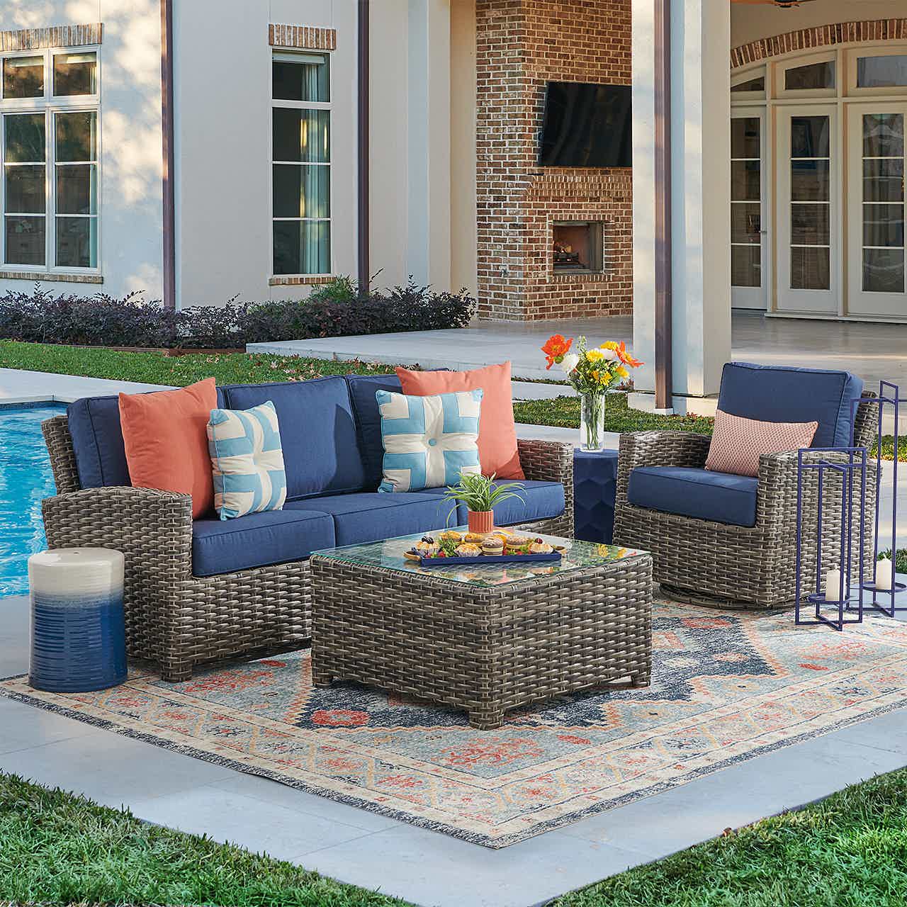 Outdoor seating area with cushions, table, and decorative elements by a pool.