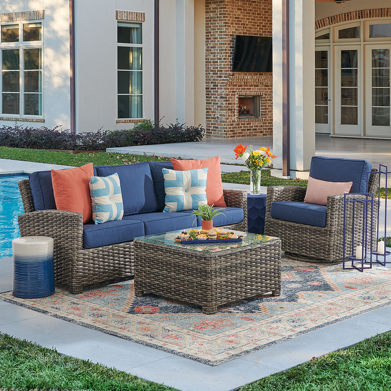 Outdoor seating area with cushions, table, and decorative elements by a pool.