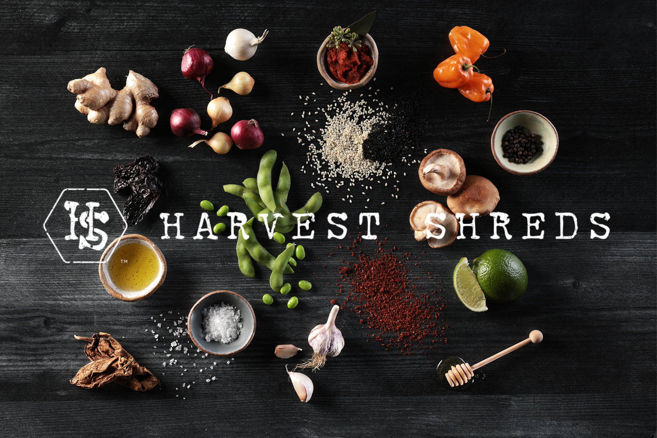 Harvest Shreds logo on a background of the components that make up this shredded plant protein, including chipotle peppers, garlic, salt, shiitake mushrooms, honey, ginger, sesame seeds, habanero peppers and red miso.