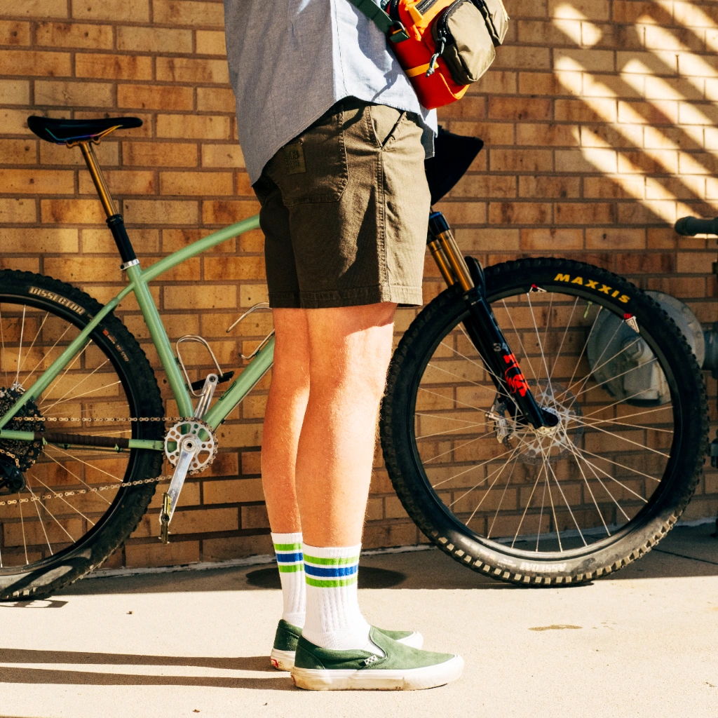 Person standing next to a bike, wearing shorts and colorful socks.