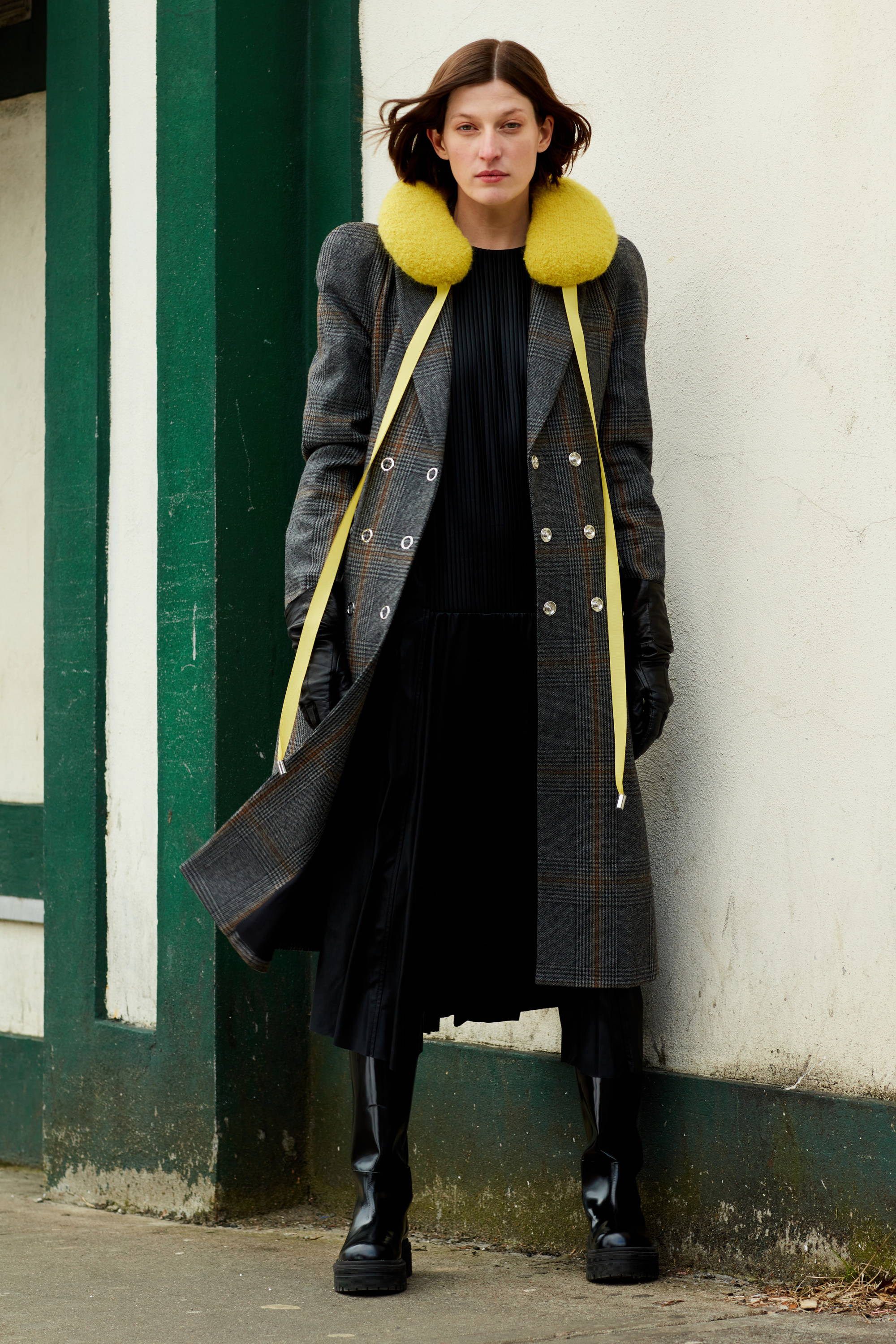 Model wearing a stylish coat with yellow accents against a plain background.