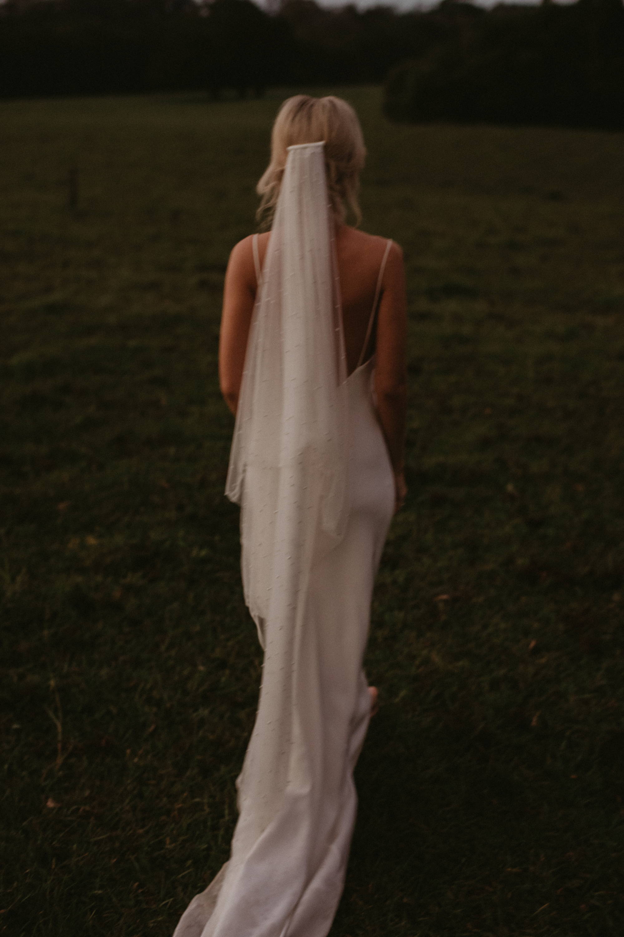 Mariée portant un long voile de tulle dans un champ d'herbe.